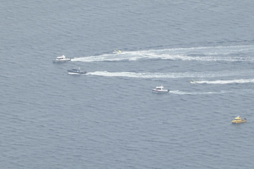 Aerial vision of boats moving across a body of water, with whitewater in their wake.