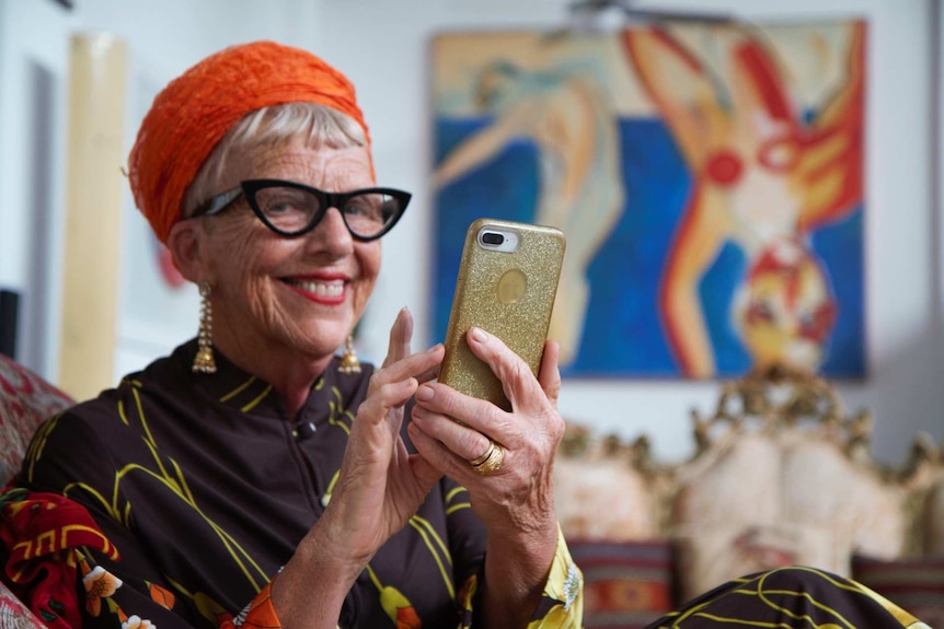 Wearing colourful clothing, Lesley Crawford sits on a couch and holds a gold sparkly iPhone.
