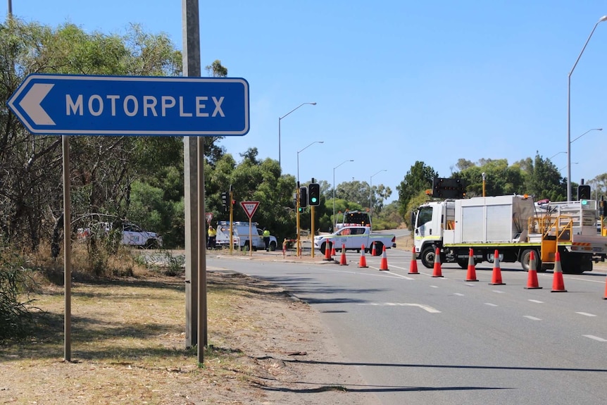 A truck and vehicles with orange cones for a roadblock near a road sign for the Perth Motorplex.