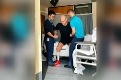 A screenshot of Michael Klim being helped up from his hospital bed by two nurses in Bali