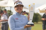A female golfer holds up a trophy after winning a mixed-gender golf tournament.