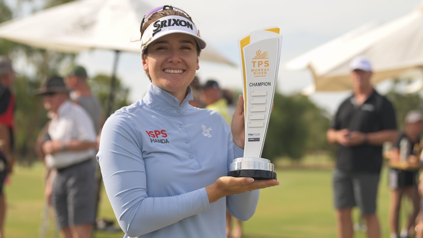 A female golfer holds up a trophy after winning a mixed-gender golf tournament.