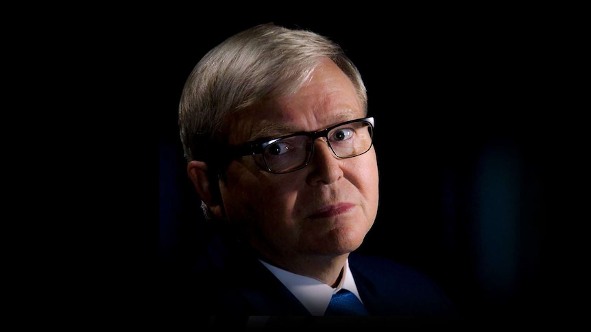 Kevin Rudd grimaces, while glancing off camera. There is a spotlight illuminating his face against a dark background.