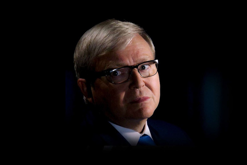 Kevin Rudd grimaces, while glancing off camera. There is a spotlight illuminating his face against a dark background.