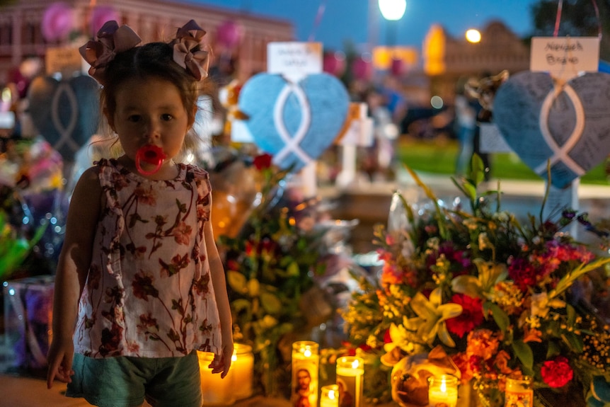 A young girl with pigtails stands in front of a memorial lit up by candles after a Texas school shooting