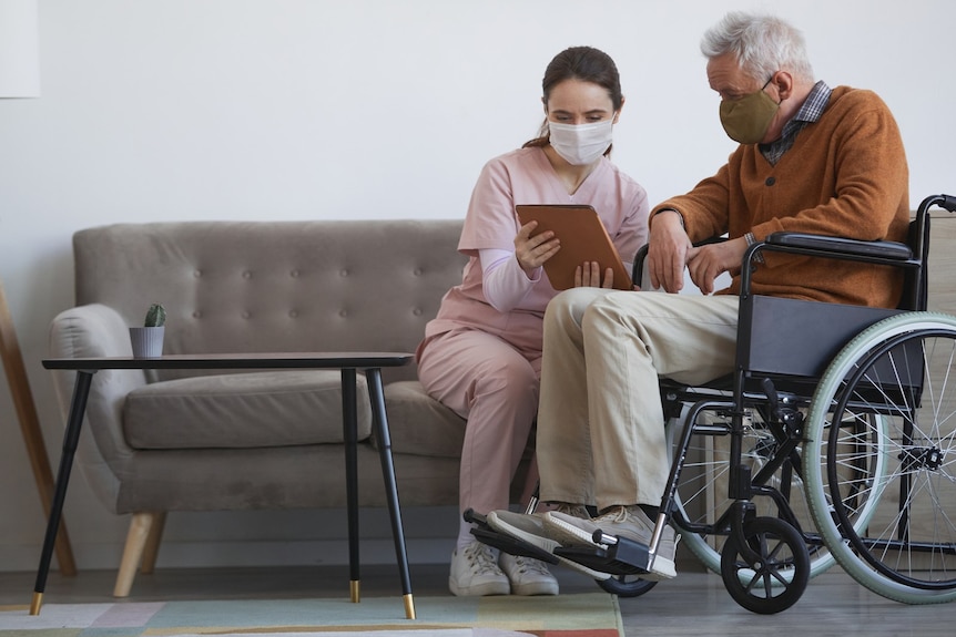 A female health worker shows documents to an older man who is in a wheelchair.