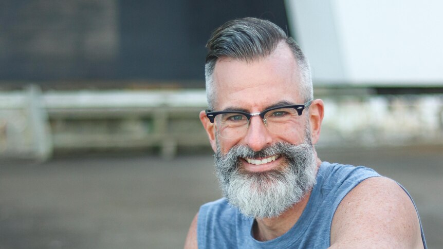 A man with grey hair and beard smiles at the camera