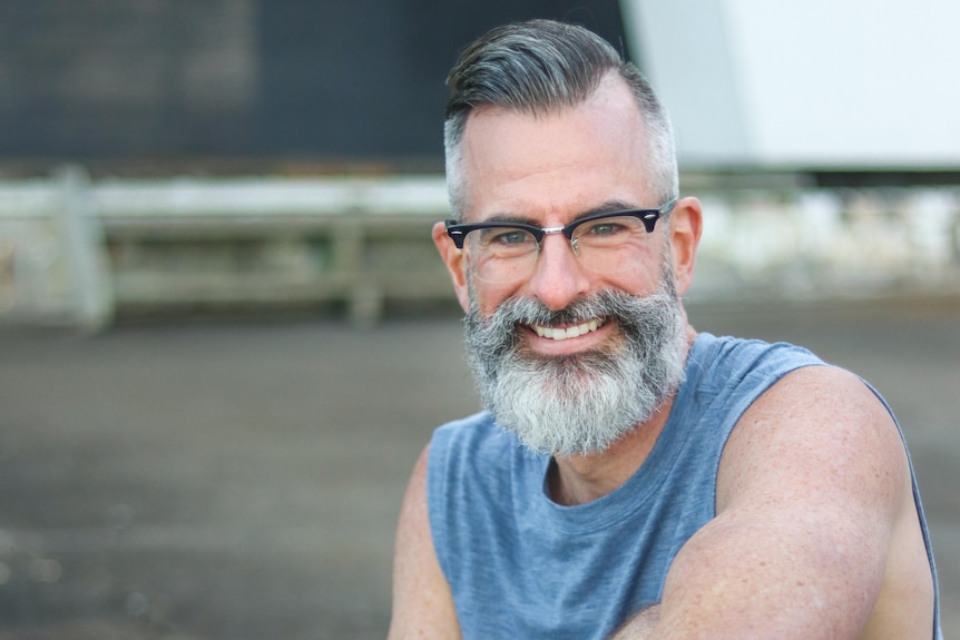 A man with grey hair and beard smiles at the camera