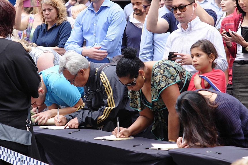 People sign condolence books near the Lindt cafe