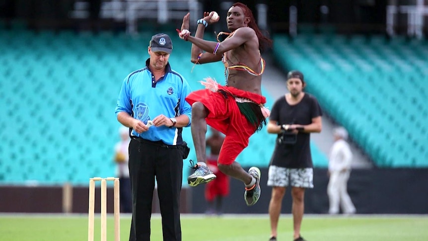 Maasai Cricket Warrior in traditional dress captured mid-air as he bowls.
