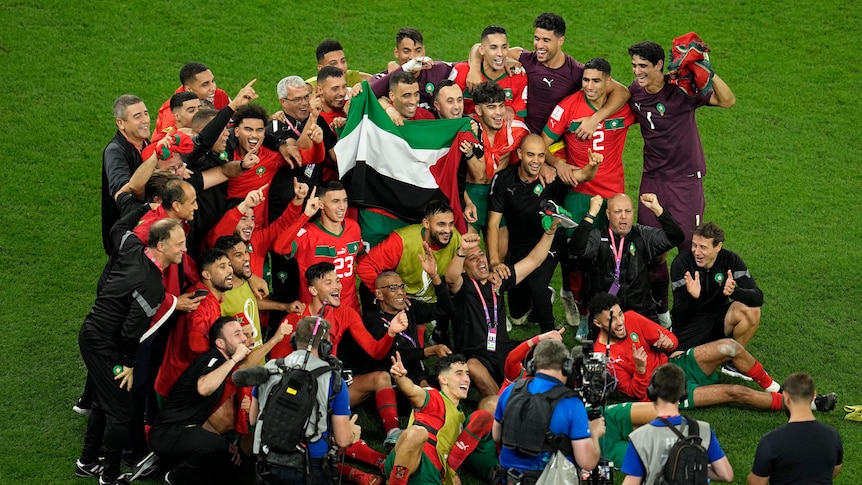 A men's soccer team wearing red and green holds up a flag during celebrations