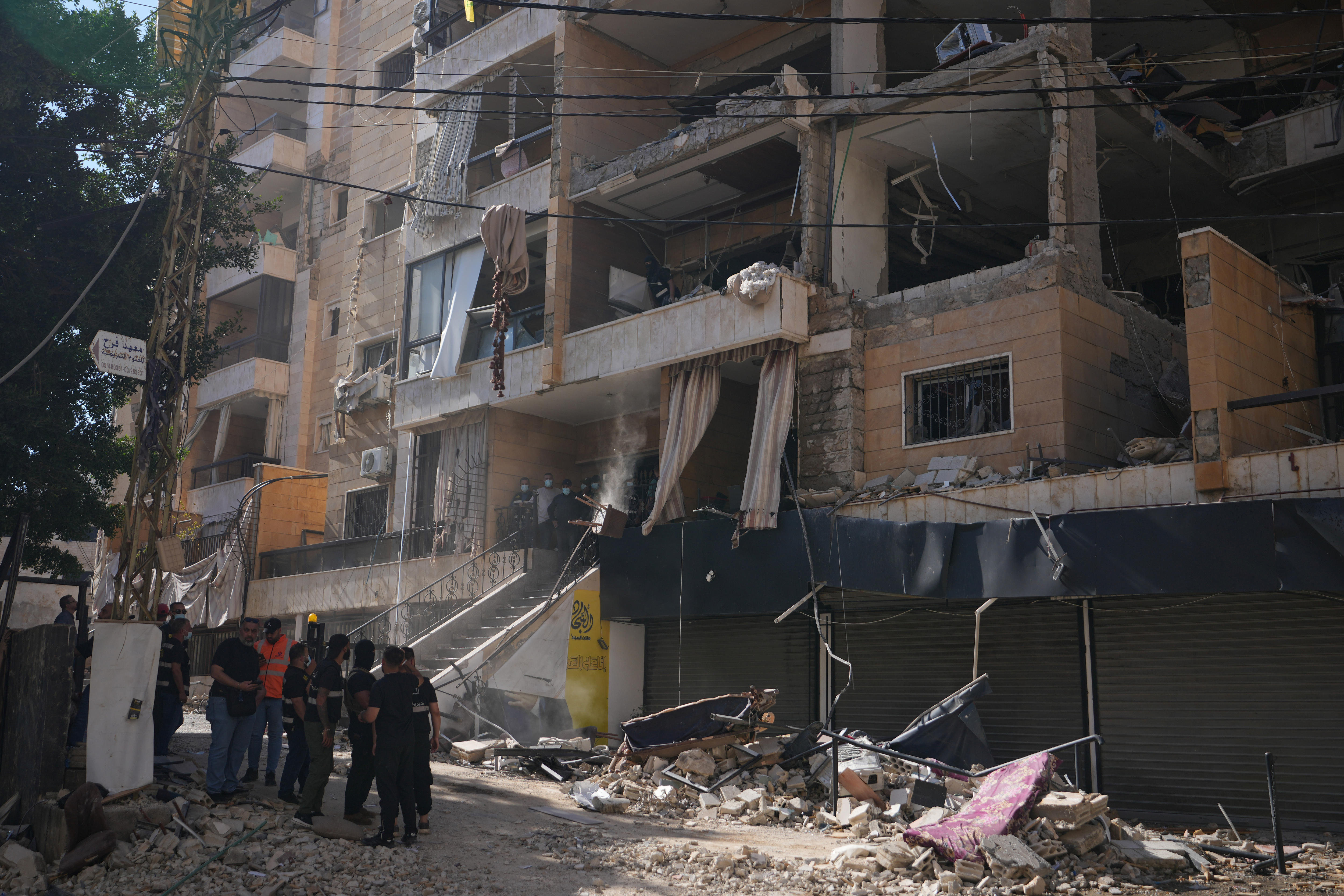 A group of people stand near rubble from a bombed apartment building.