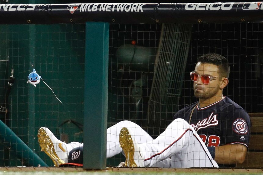 Gerardo Parra sits wearing sunglasses and his feet up on a ledge with a small toy shark hanging from some netting