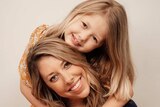 Daughter cuddling mother and smiling at camera, pictured in story about single parents in isolation