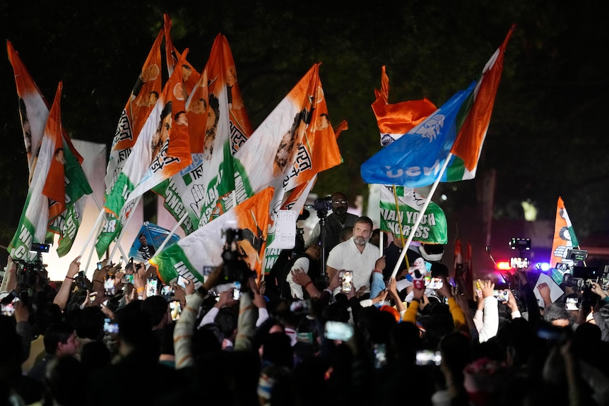 An Indian politican is surrounded by flag-waving supporters at night.