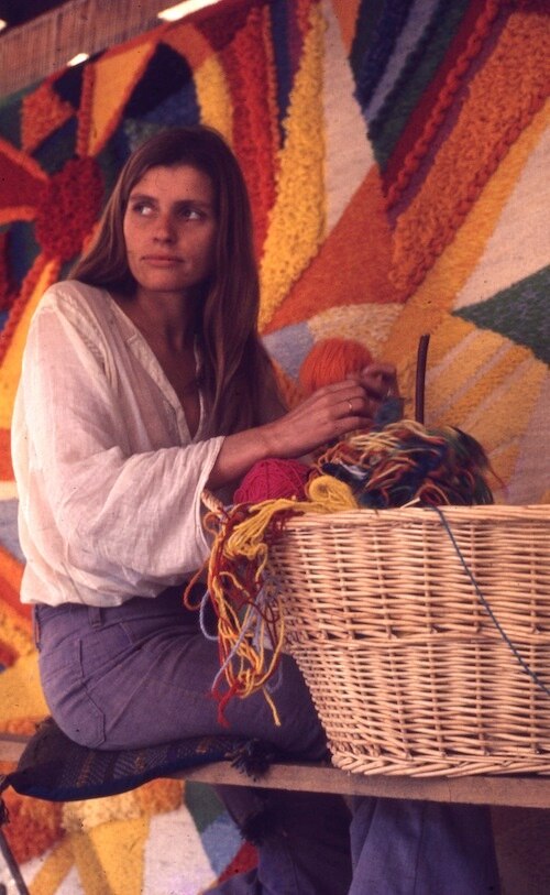 A woman sits making her tapestry wall hanging.