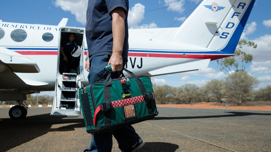 A clinician holding a medical bag stands on the tarmac in front of a Royal Flying Doctor airplane
