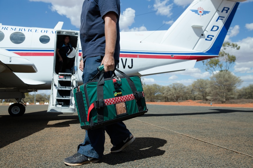 A clinician holding a medical bag stands on the tarmac in front of a Royal Flying Doctor airplane