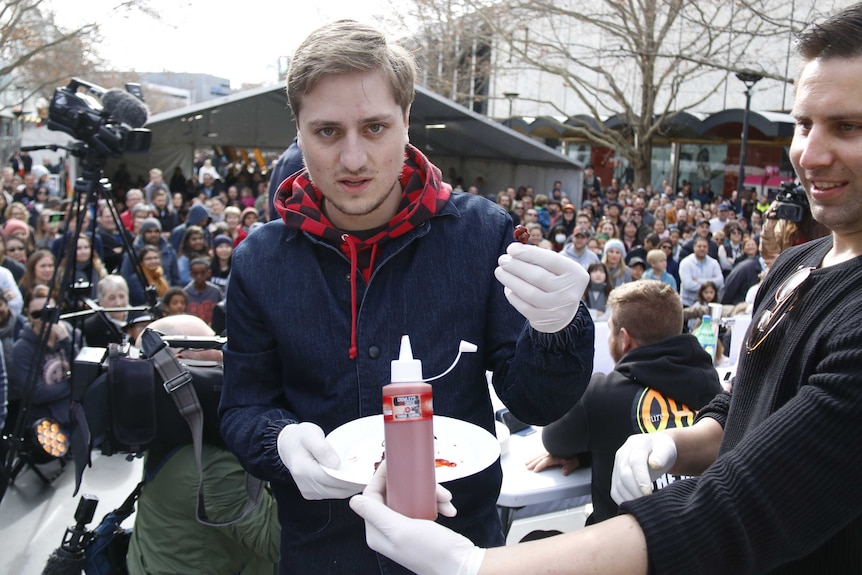 A man holds up a small dried chilli.