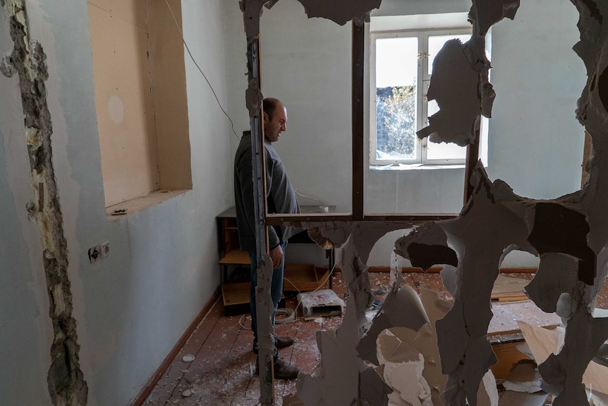 A man stands in a half demolished room, looking around at the damage
