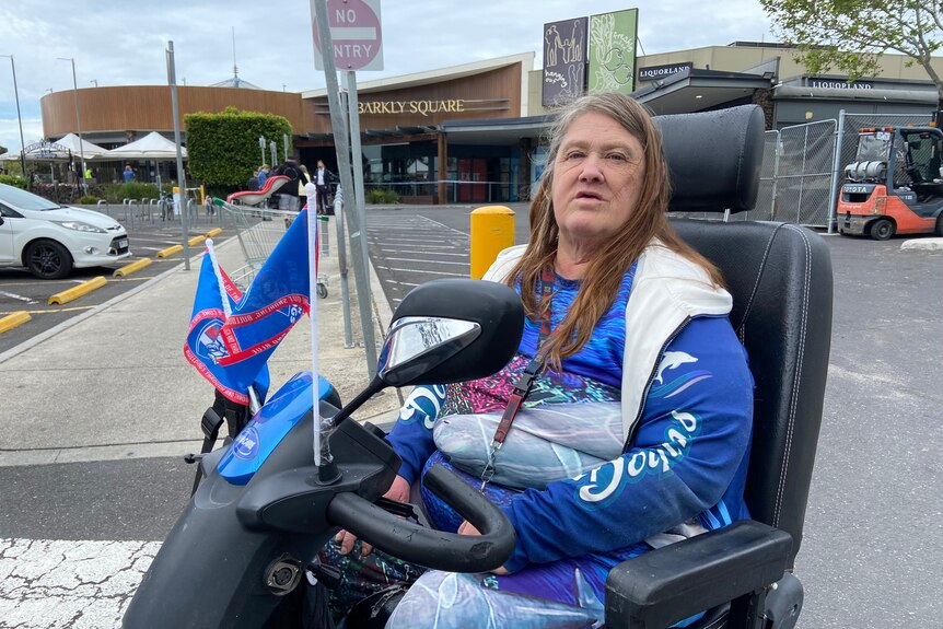 Woman in blue jumper sits at mobility scooter with flags on the front of it.