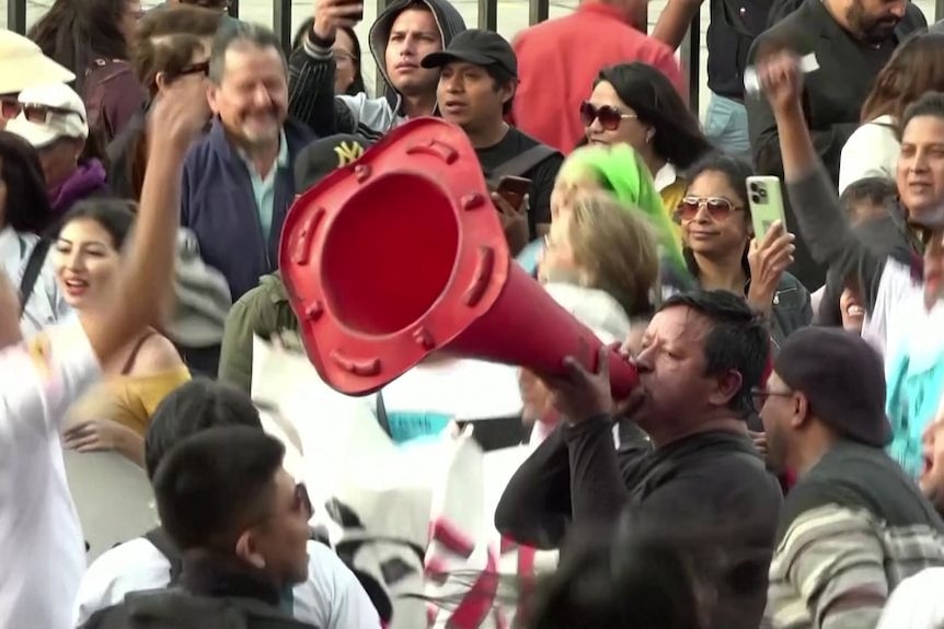 A man in a crowd yells through a witch's hat.