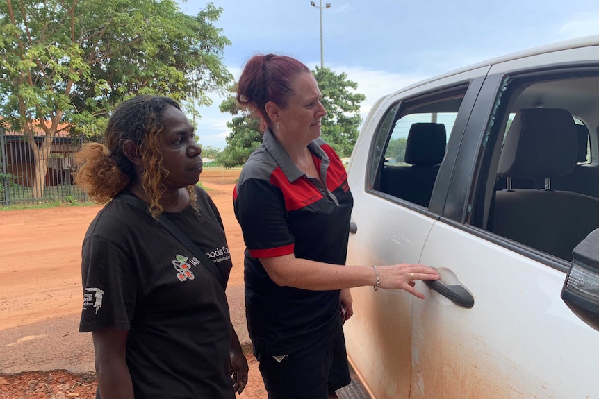 Two women in Bawinanga Aboriginal Corporation t-shirt and polo shirt inspect broken windows on the side of a ute.