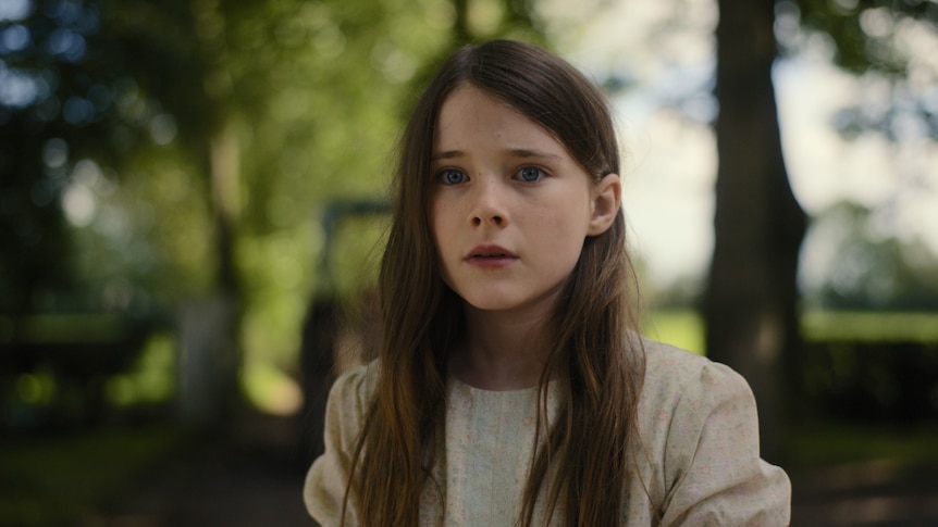 A young girl with long brown hair stares, mortified, into the distance