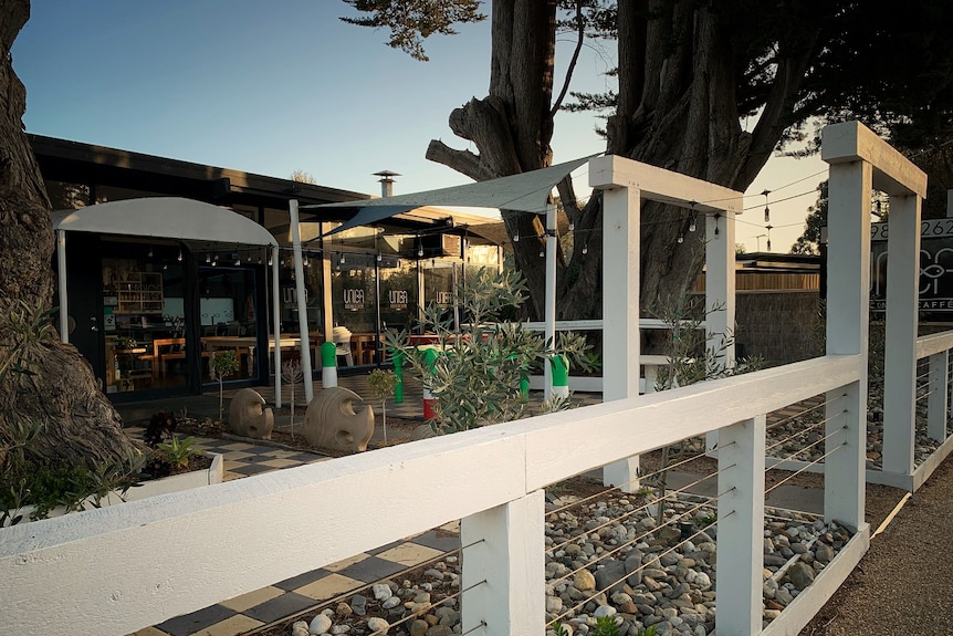The outside of a restaurant by the coast at sunset, with white wooden posts forming an arched walkway.
