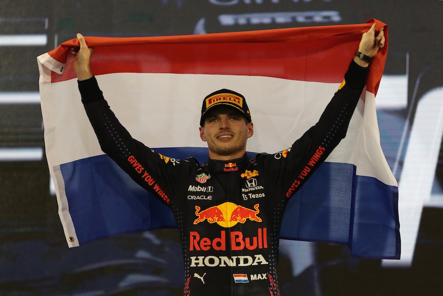 Victorious race car driver on the podium holding a flag of the Netherlands.