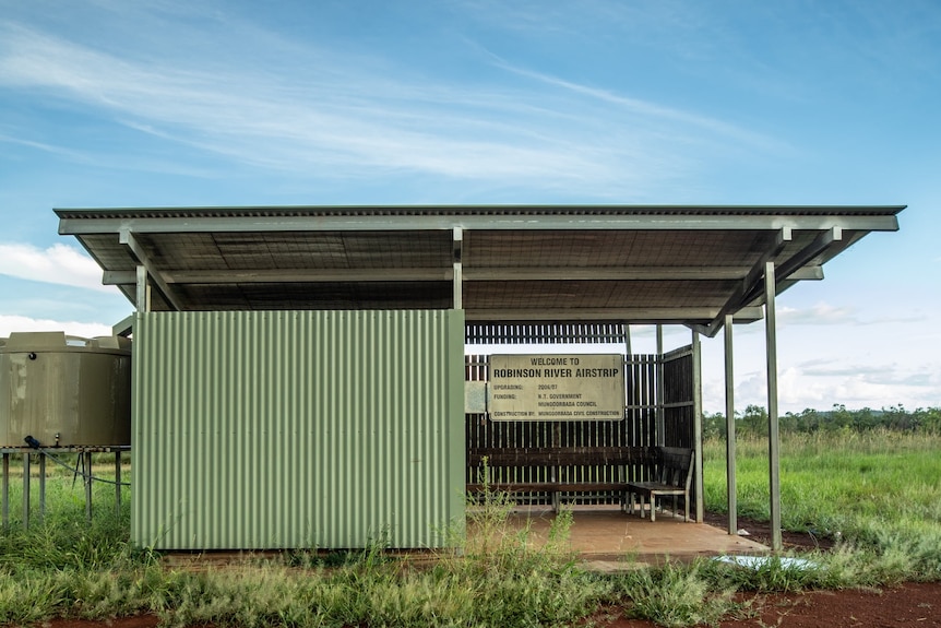 A green bus shelter can be seen in the middle of nowhere. Blue skies are behind.