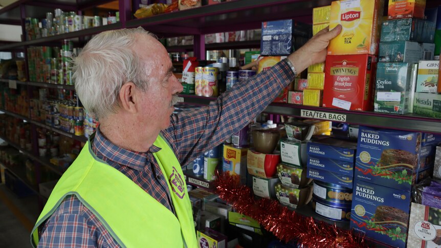 A man with grey hair placing a box of teabags on a stocked shelf in a warehouse.