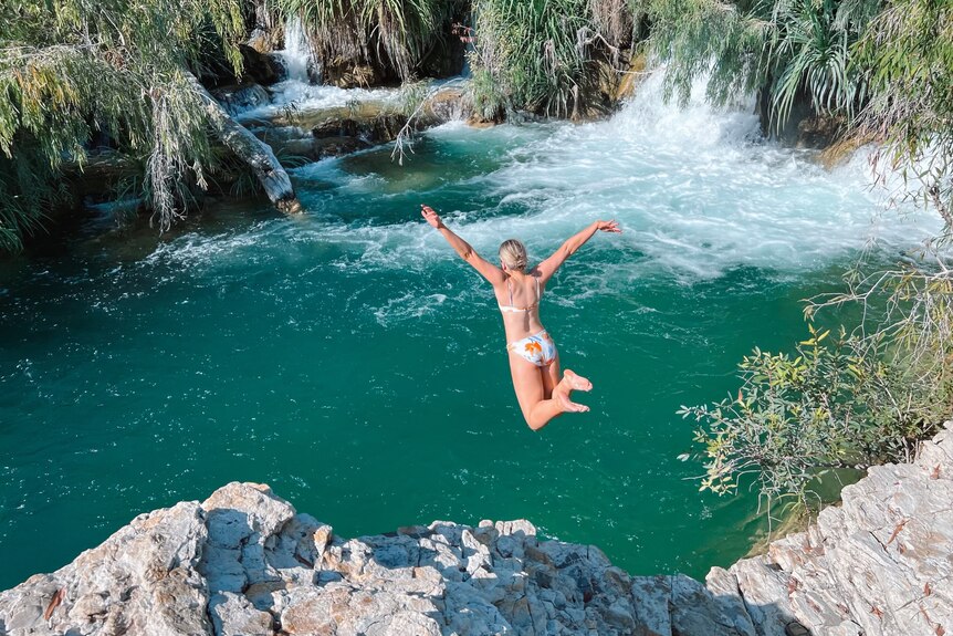 A woman in swimsuit jumps into a water hole