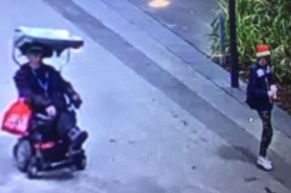 Grain vision of a man in an electric wheelchair with red shopping bags attached and a man wearing a Santa hat.