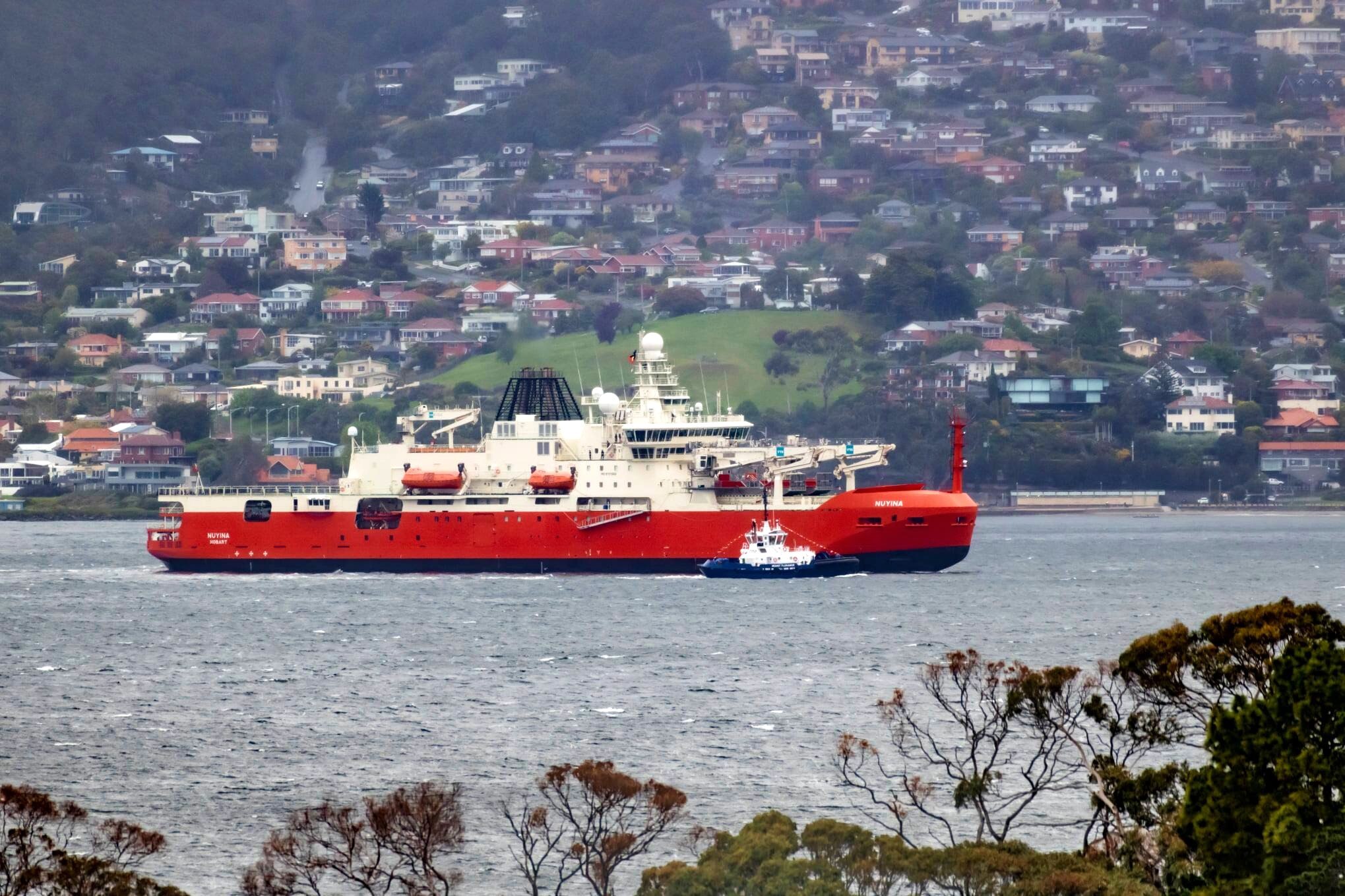 A white and orange ship on a river with houses in the background