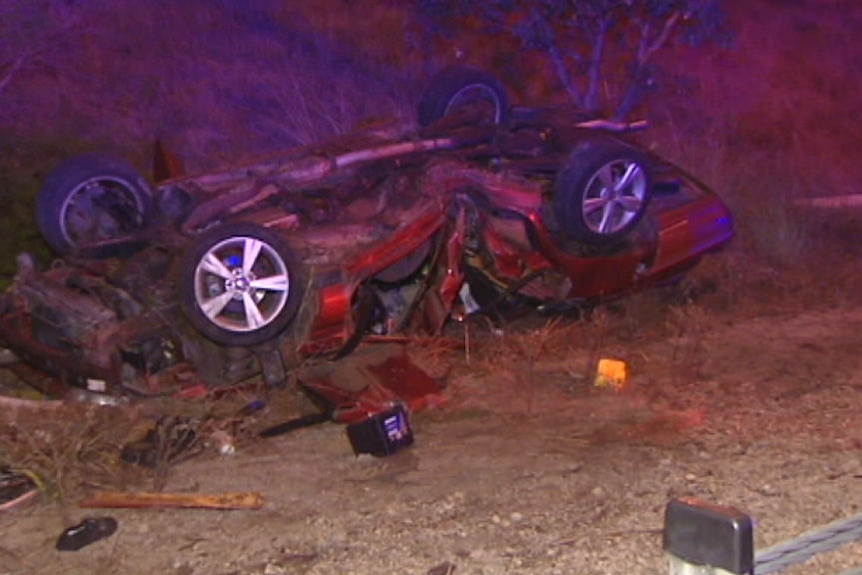 The wreckage of a crashed car lies crumpled on the side of a road.