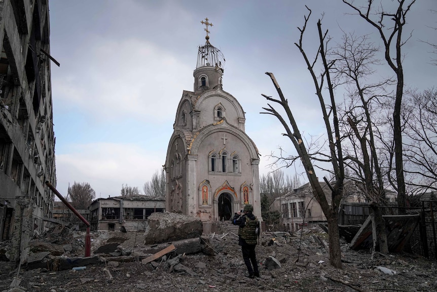 A man looks at church standing among debris