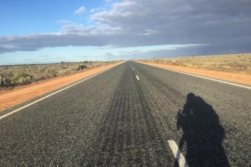 A cyclist casts a long shadow on the open road.