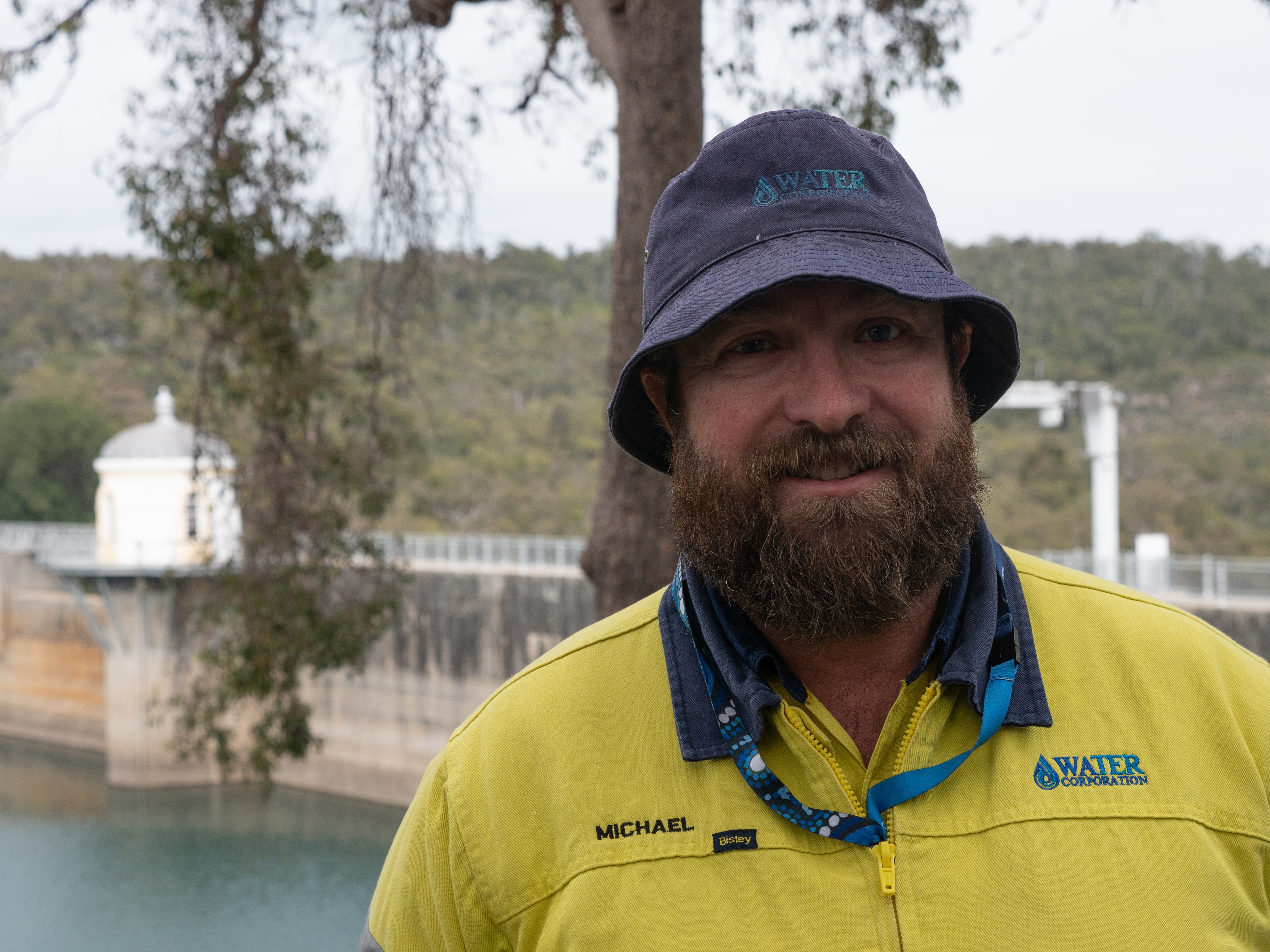 Man in bucket hat and yellow high-vis with dam in background