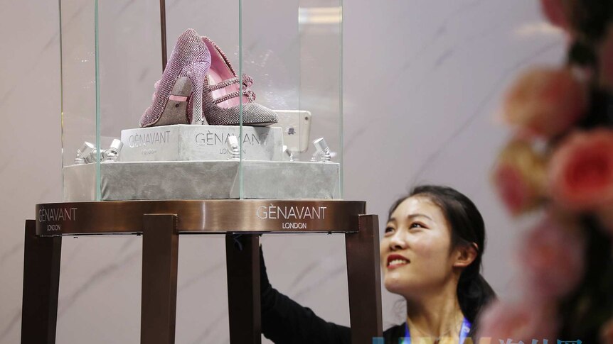 A woman looks at a pair of pink diamond encrusted shoes in a glass display cabinet.