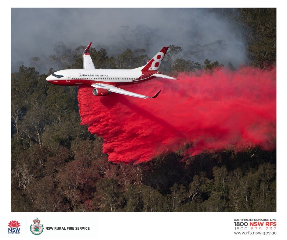an air tanker plane from the nsw rural fire service flying over a bushfire dropping red fire retardant