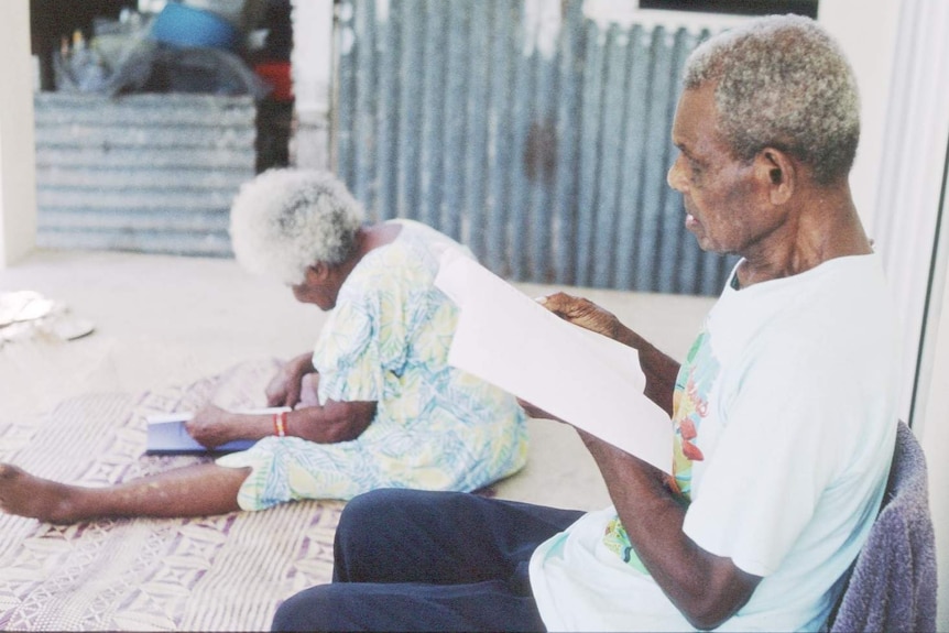 Two elderly people in Vanuatu reading books in their local language.