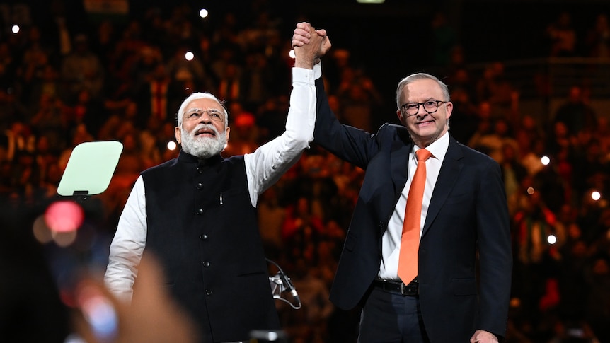 Two men link hands and hold their arms up to a large crowd