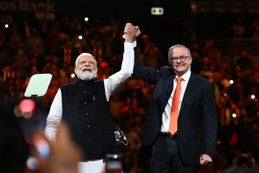 Two men link hands and hold their arms up to a large crowd