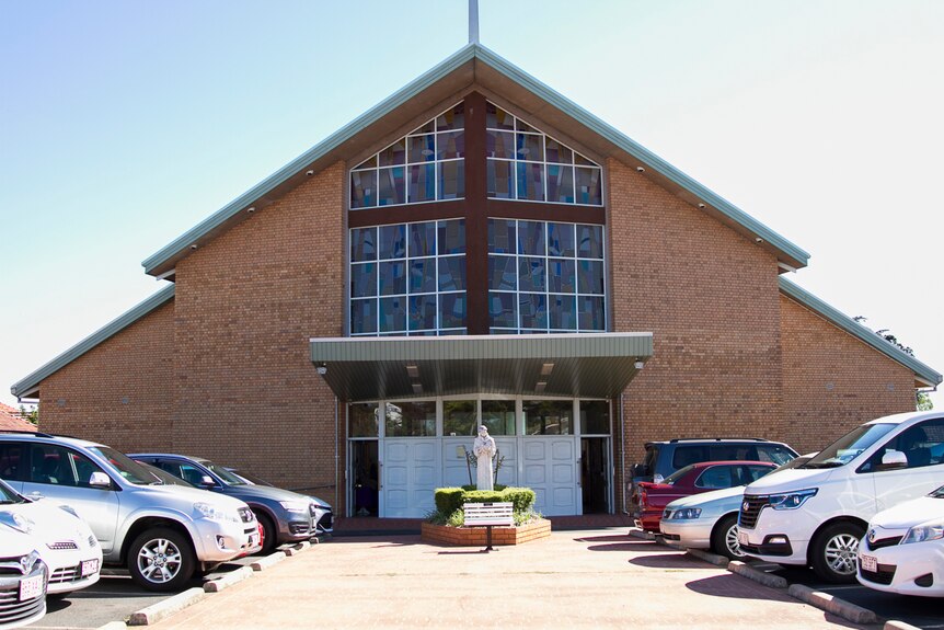 Wide shot of the brick exterior of a church, with parked cars out the front.