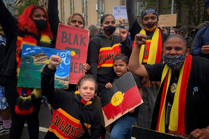 A group of protesters dressed in the red, black and yellow colours of the Aboriginal flag amongst a crowd of protesters.