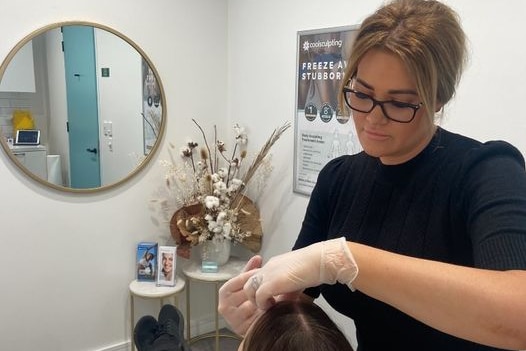 Woman wearing black t-shirt, glasses and plastic gloves places her hands on a persons forehead