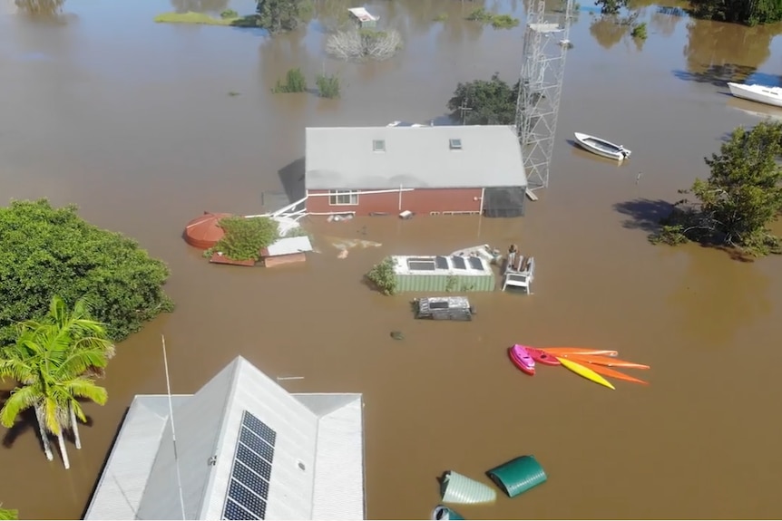 aerial showing high flood waters surrounding a home with solar panels and shed, kayaks and canoes