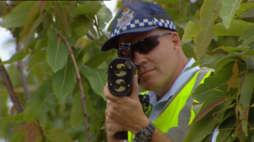 TV still of close-up of anonymous Qld police officer with a speed camera in Brisbane.