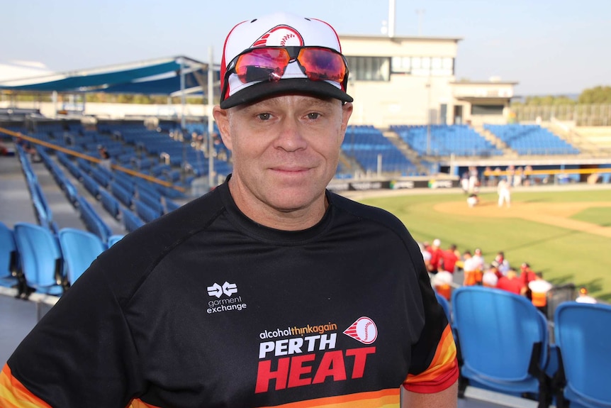 A mid shot of Perth Heat manager Brooke Knight standing in front of a baseball field wearing a Heat shirt and cap.